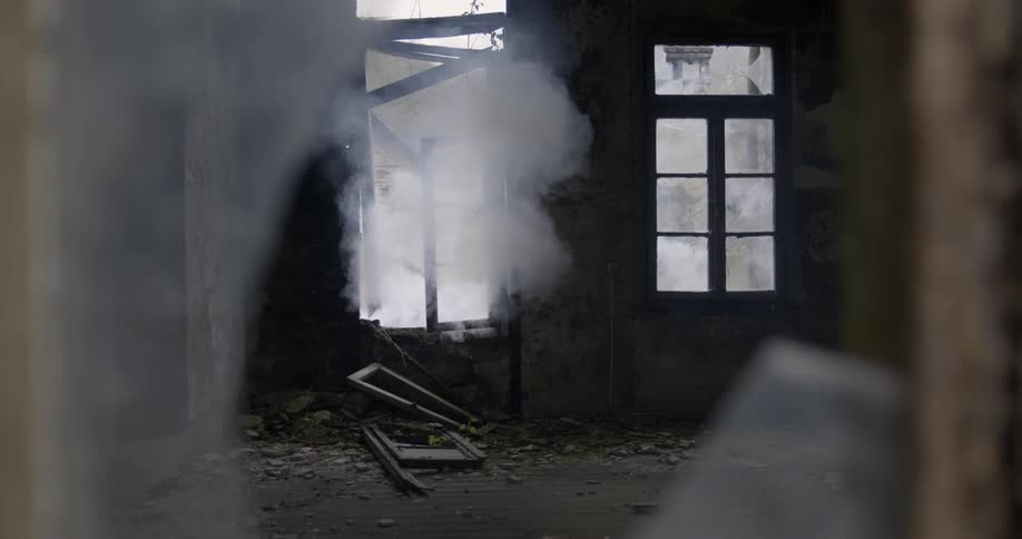 Smoking is billowing through a broken window in an abandoned house