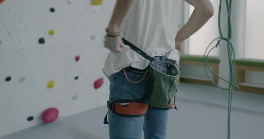 Man puts chalk on hands next to a rock climbing wall