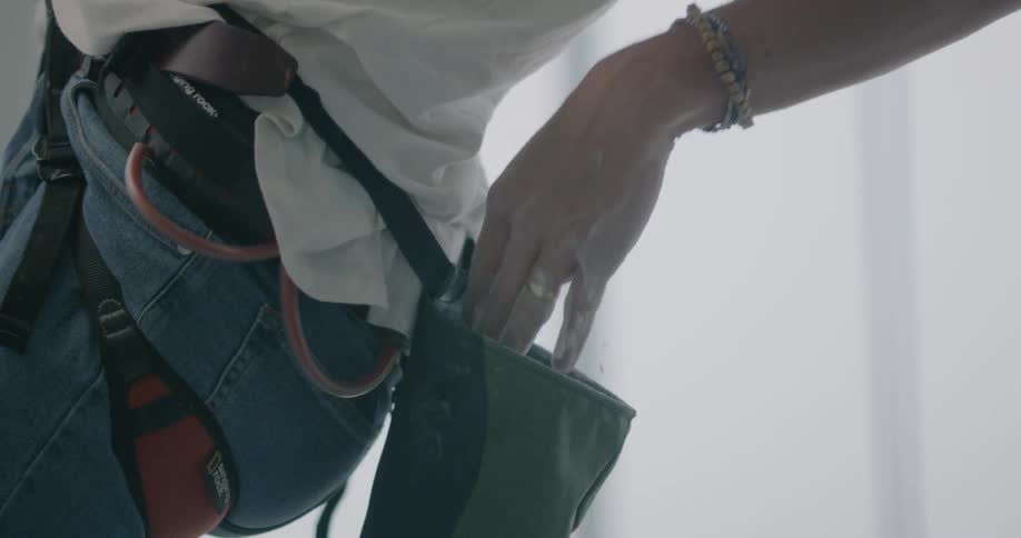A woman is pulling her hand from a chalk bag as she is suspended in a harness