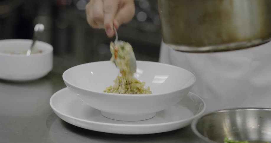 A chef is plating food from a pot in a bowl as he prepares a dish for service
