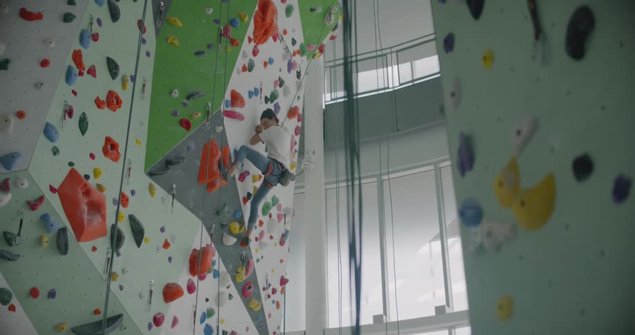 A woman climbs up a rock climbing wall