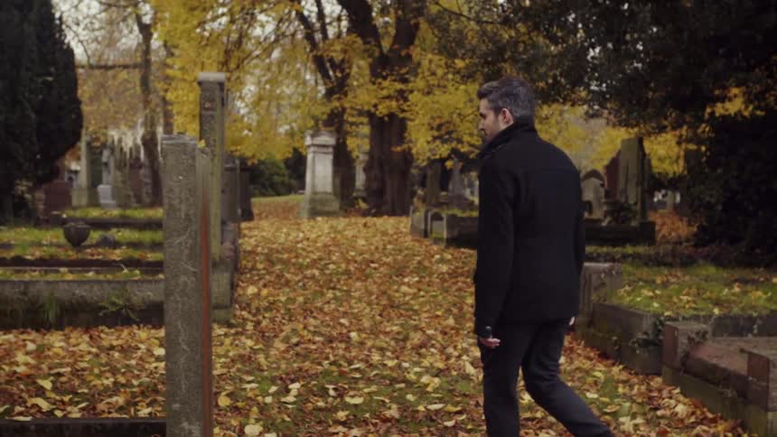 A man walks over the dead leaves in a cemetery