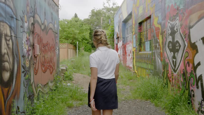 A young woman walks in a graffiti filled alley