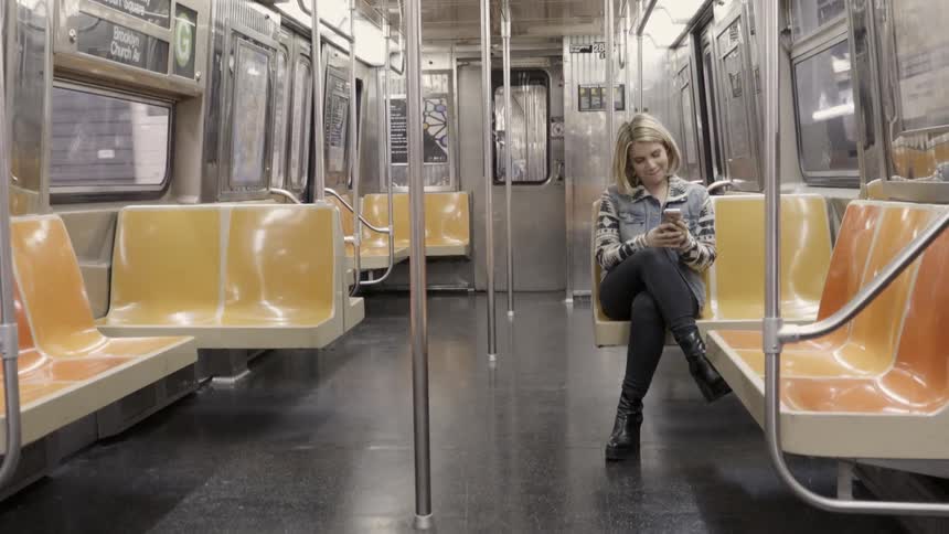 Woman riding on subway train is smiling while looking at cell phone