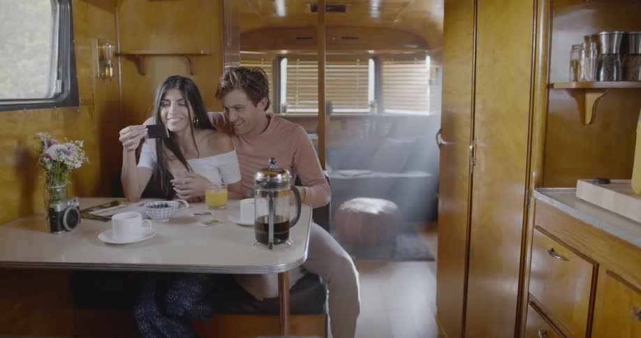 A woman is looking at a picture as she sits at a table in a trailer with a man