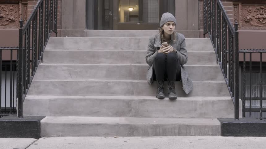 A woman uses her phone on the steps of her home