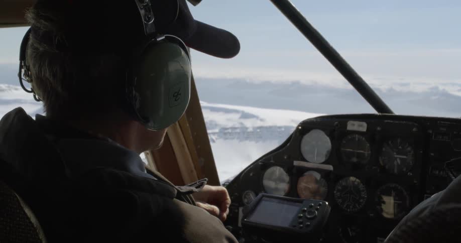 A pilot is flying a plane over snow-capped mountains on a sunny day