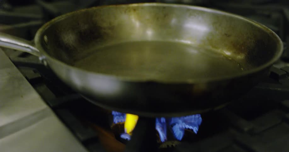 A chef pours oil into a pan on a stove