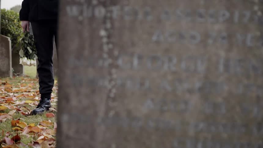 A person holds flowers in front of a grave marker