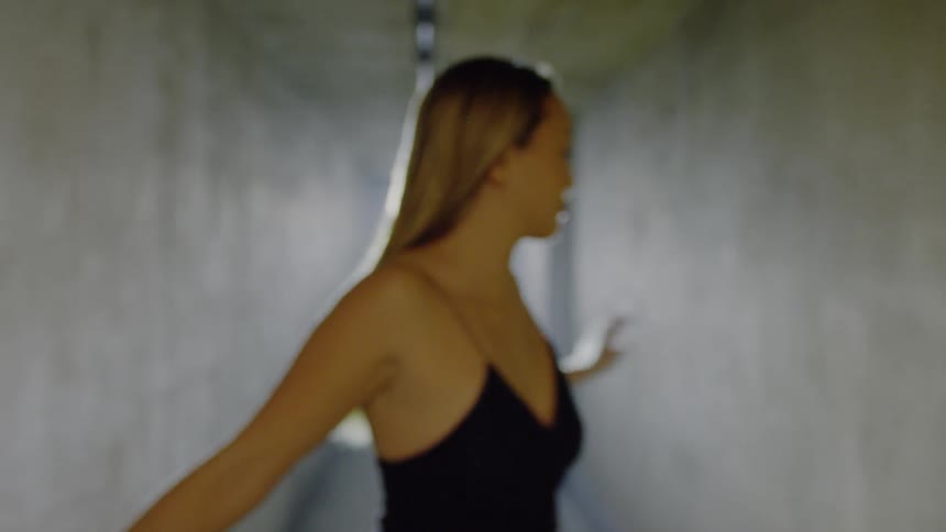 A woman dances  through a concrete hallway
