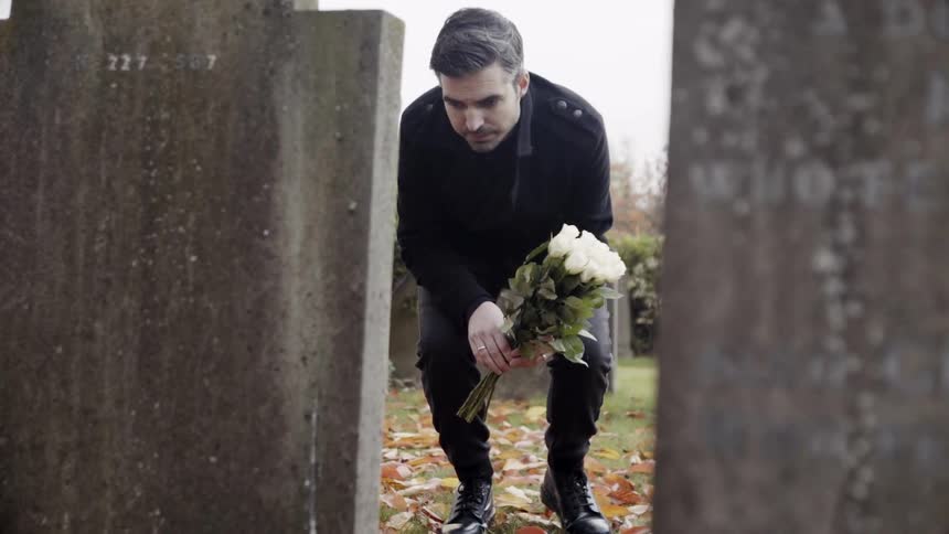 A man with flowers is kneeling down on someone's grave