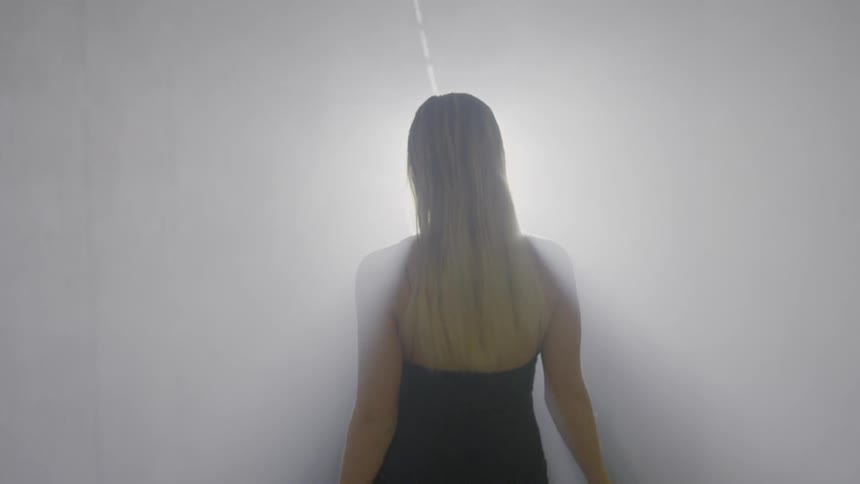 A blond woman walks down a white hallway
