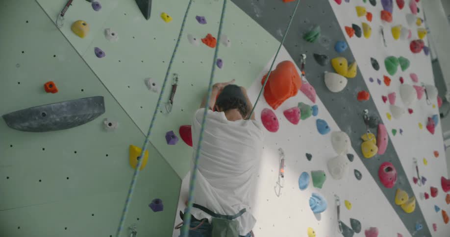 A man is climbing up a rock climbing wall in a gym
