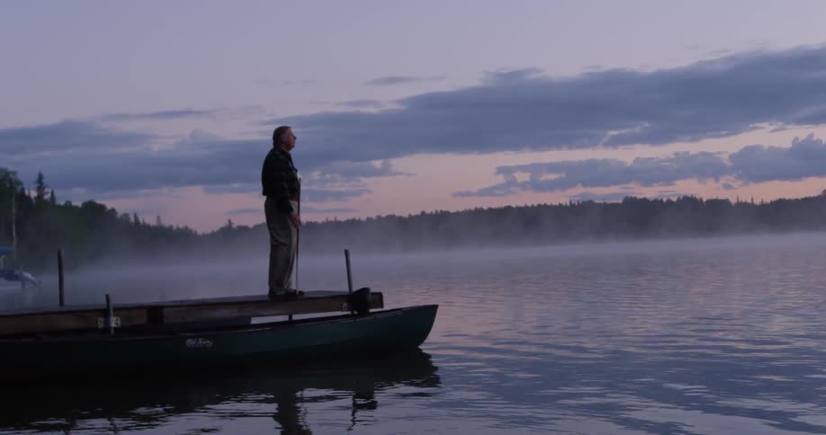 A man stands on the docks near a fog covered lake