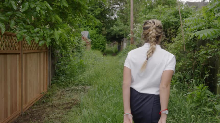 A woman is walking down an alley overgrown with grass and plants