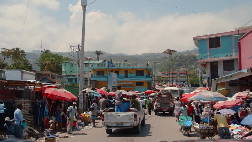 Vehicles drive down the street lined with vendors and people