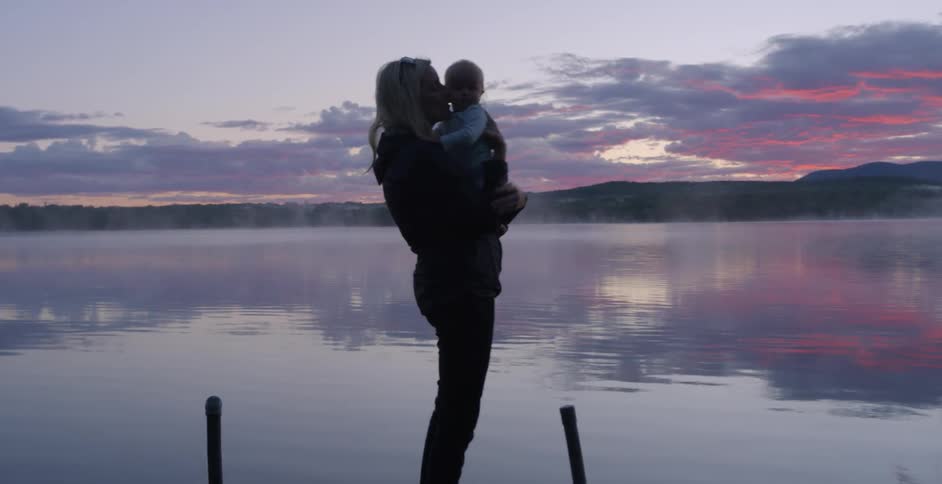 A woman kisses her baby by the lake