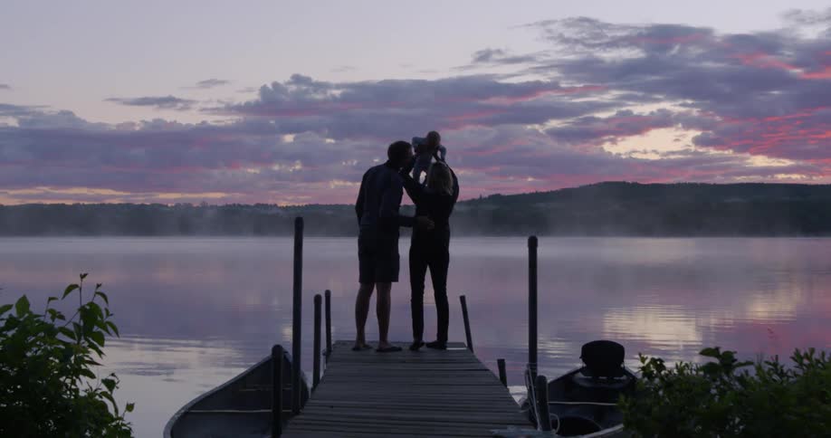 A family stands on a lake dock at sunset