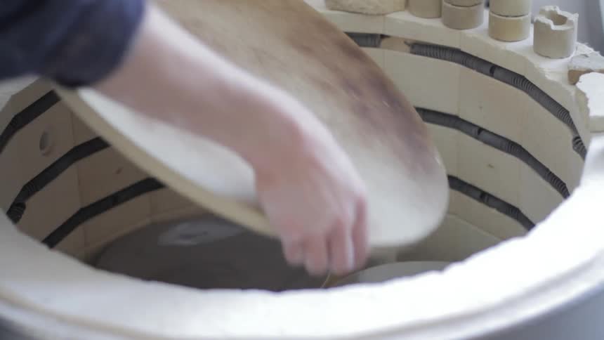 Hands shown removing a platform from a ceramics/clay firing oven