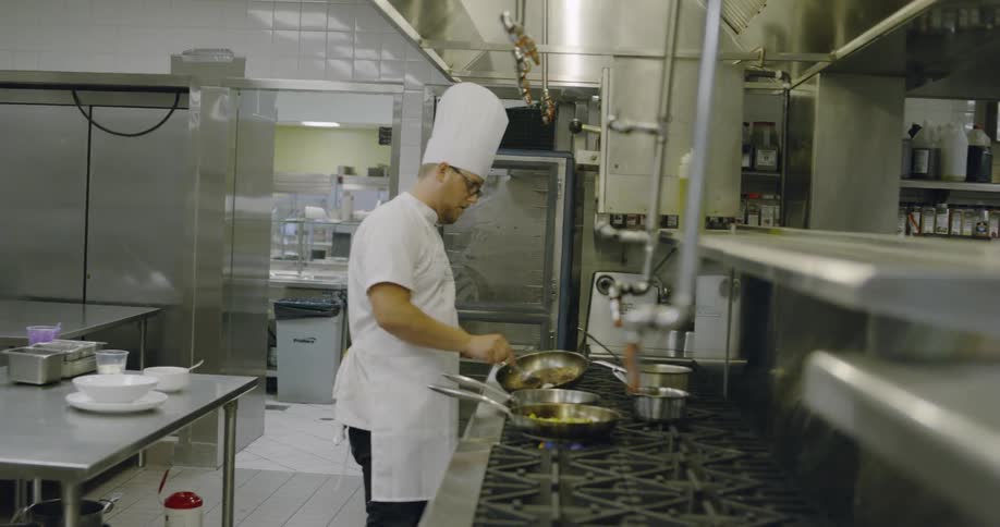 A chef is preparing food in pans on a large stove top