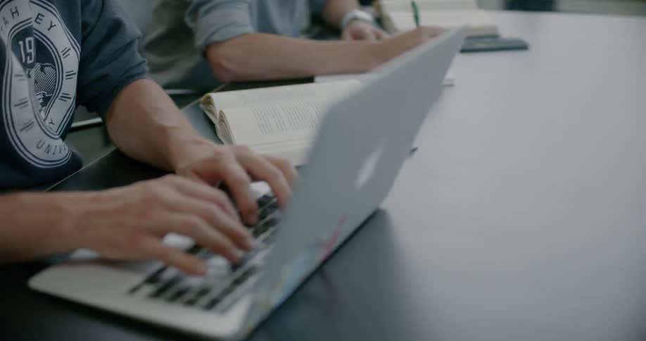 A group of people are sitting at desks using computers and notebooks