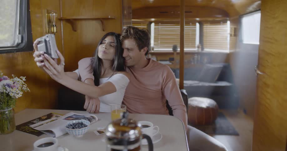 A woman and man sitting inside a camper trailer are taking a photo