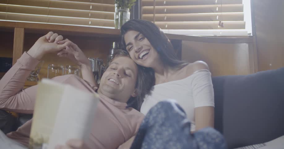 A man and woman sit on the couch laughing