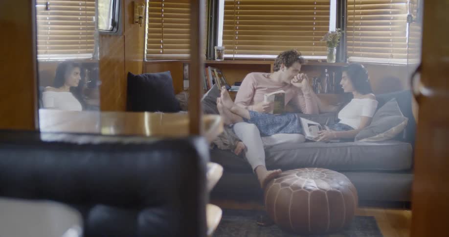 A boy and girl are sitting on a couch talking and the girl has her legs over the mans lap