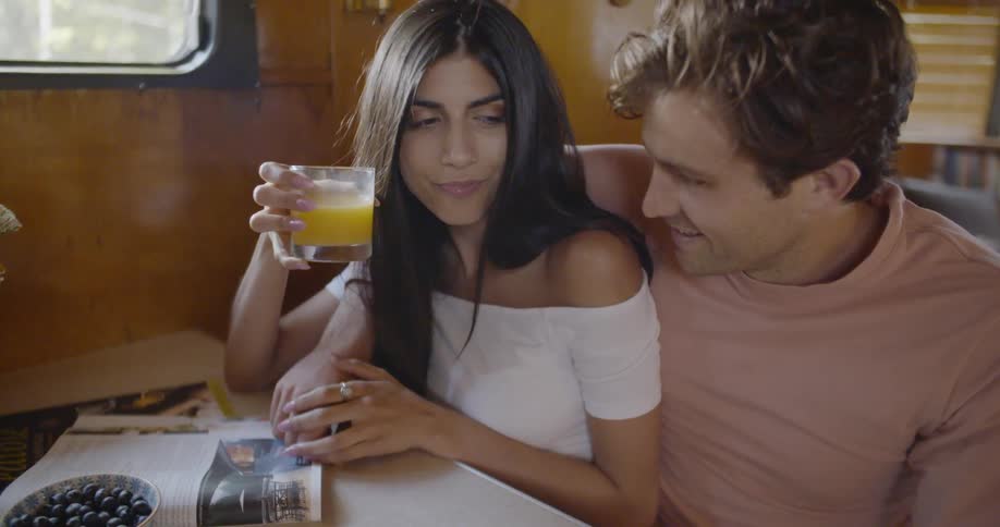 A woman is drinking orange juice as she sits with a man in a camper trailer