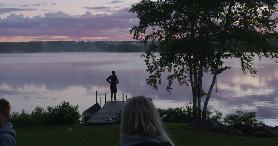 People walk towards a dock where a man stands looking out at the lake