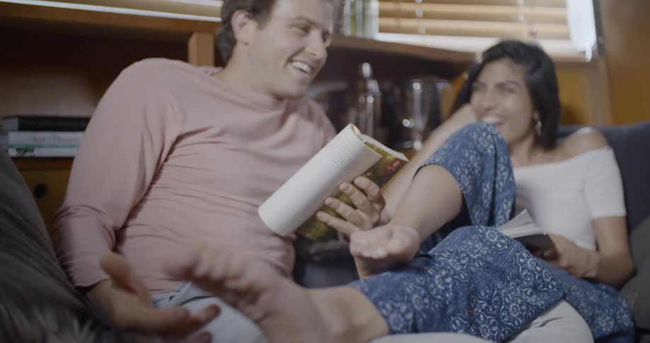A man and woman laugh while reading on a couch