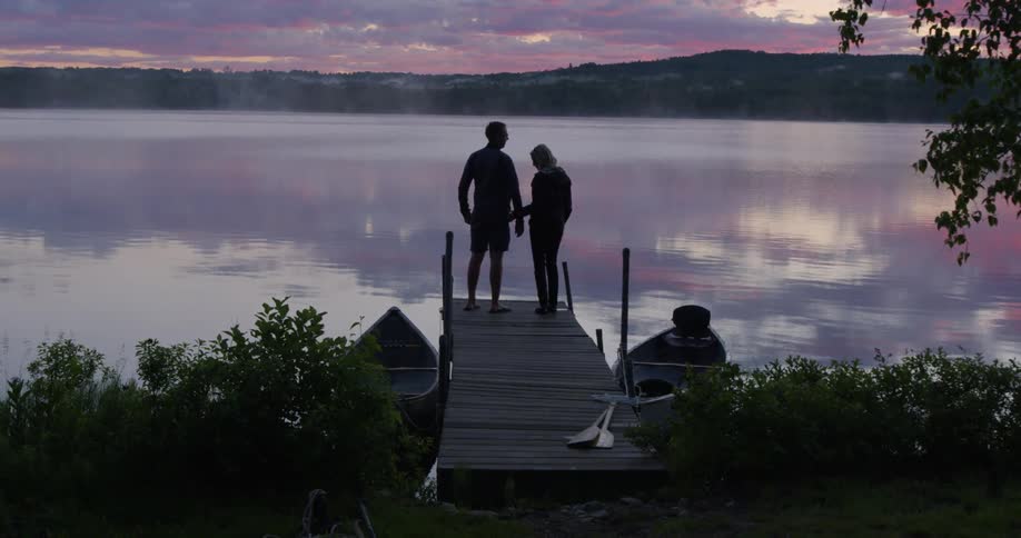 Two people stand together on the pier watching the sun set
