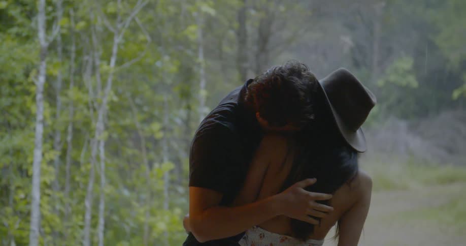 A man and woman hug next to trees