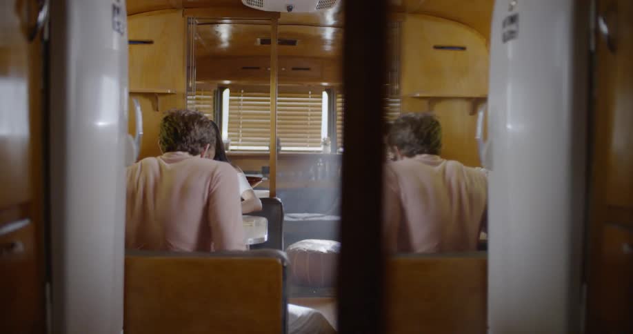 A man sits down opposite a woman at a table in a camper trailer
