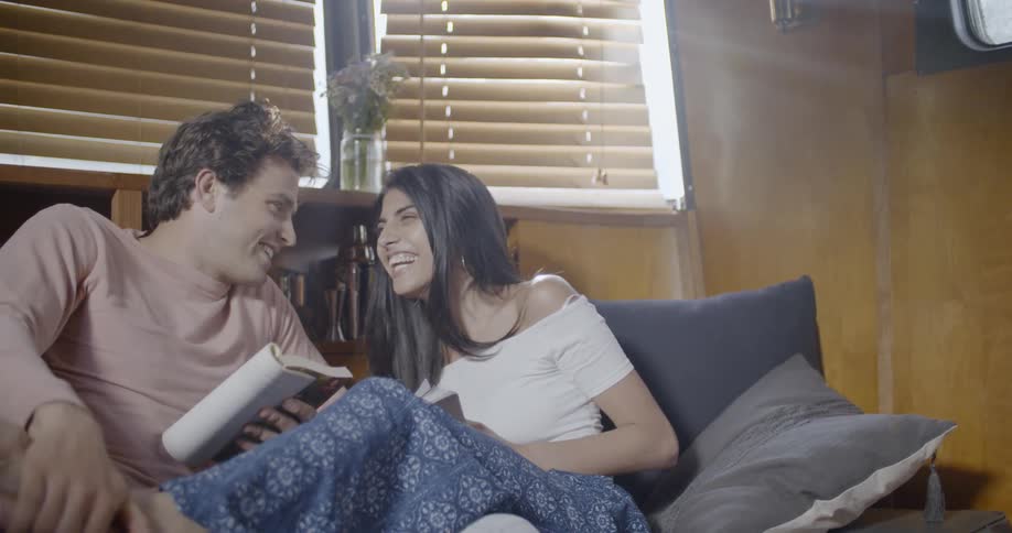 Man and woman laugh while reading on a couch