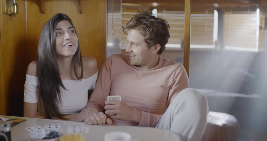 A man and woman laugh and talk as they sit close to each other at a table indoors