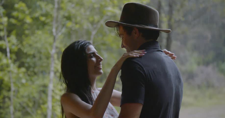 Man hugs woman as she puts hat on his head and smiles