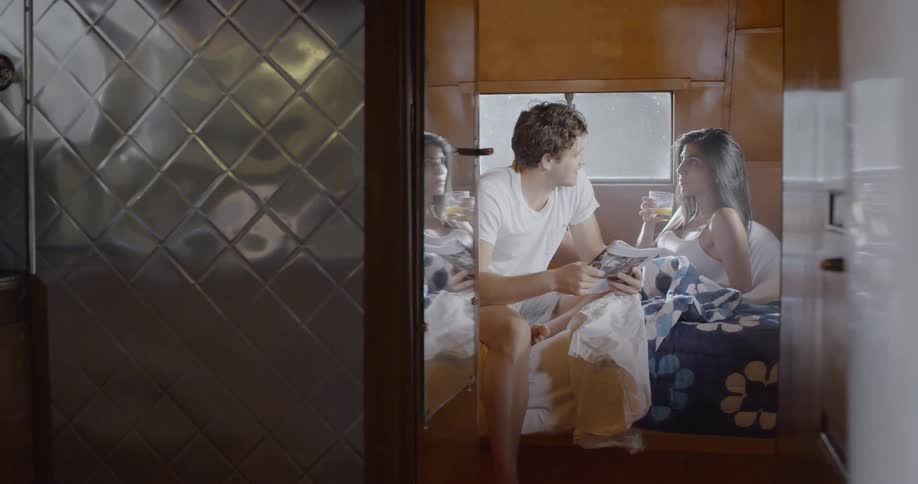 A man and woman sit in bed enjoying a morning in a camper van