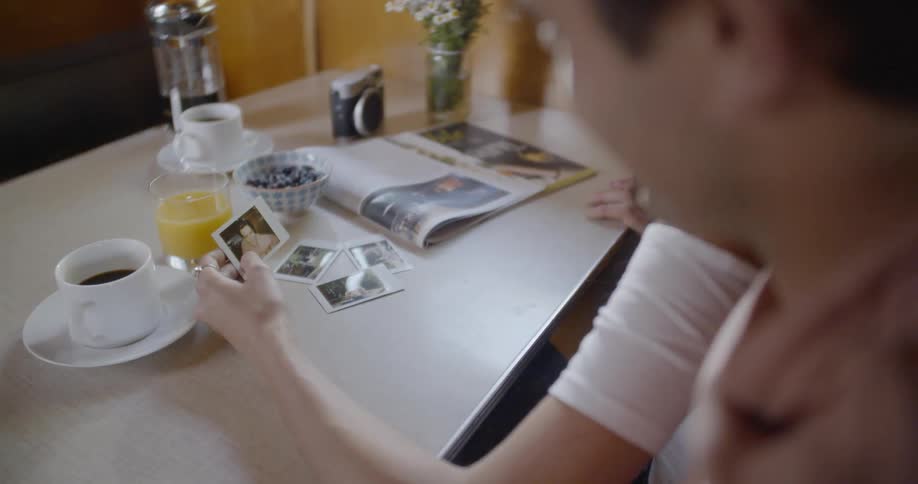 Man drinks coffee while looking at photographs with a woman