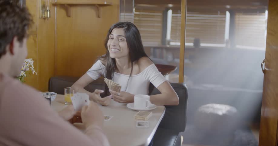 A woman is laughing and talking while playing cards with a man at a table