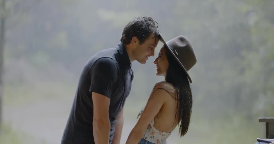 A man and woman lean forward embracing as it rains outside