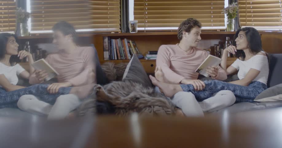 A girl and guy are sitting on the couch together reading a book