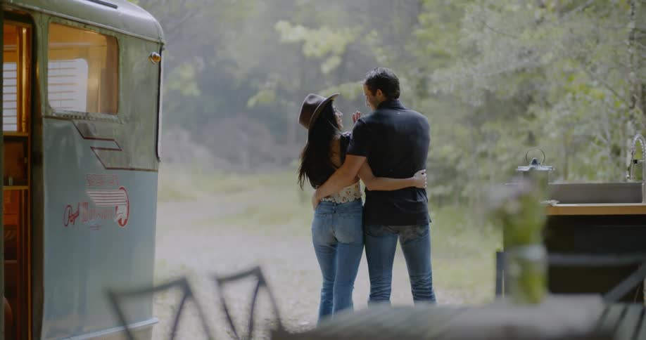 A couple are standing outside next to a trailer camper during the day