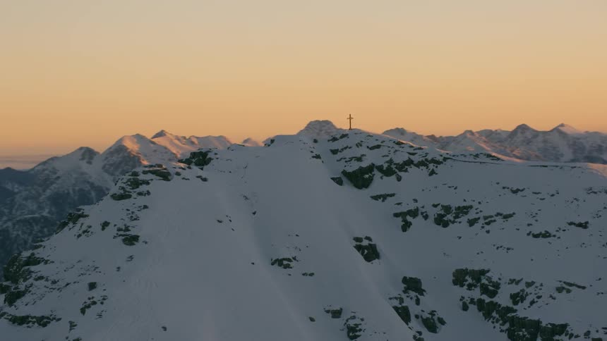 There is a cross on the snow covered mountain at sunset
