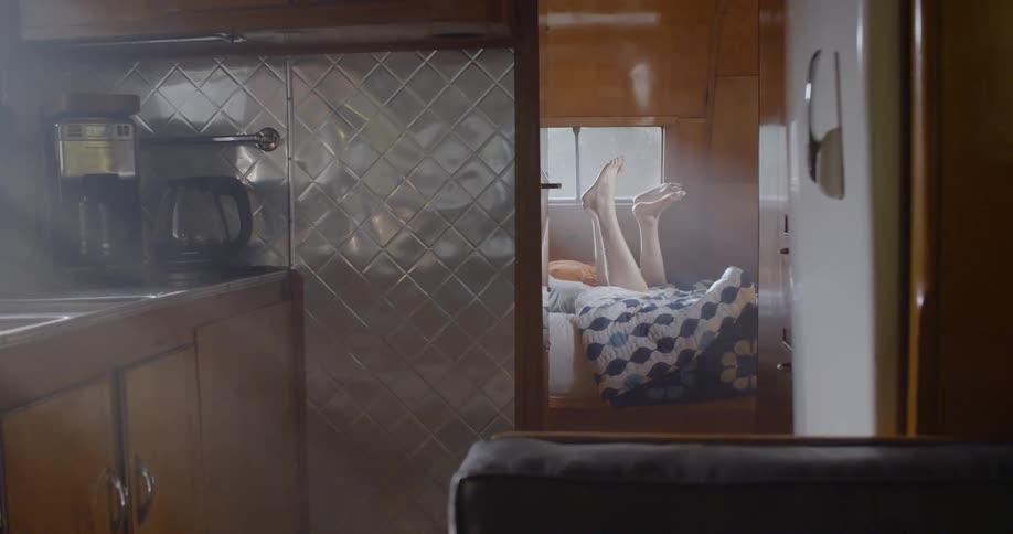 A man and woman laying on a bed in a trailer are kicking their legs