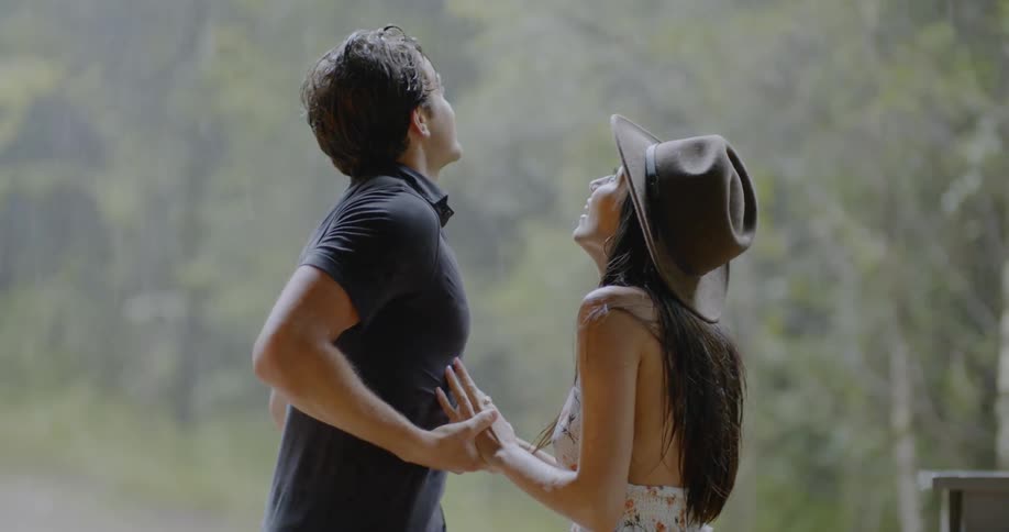A man and woman hold hands as they look up at the rain