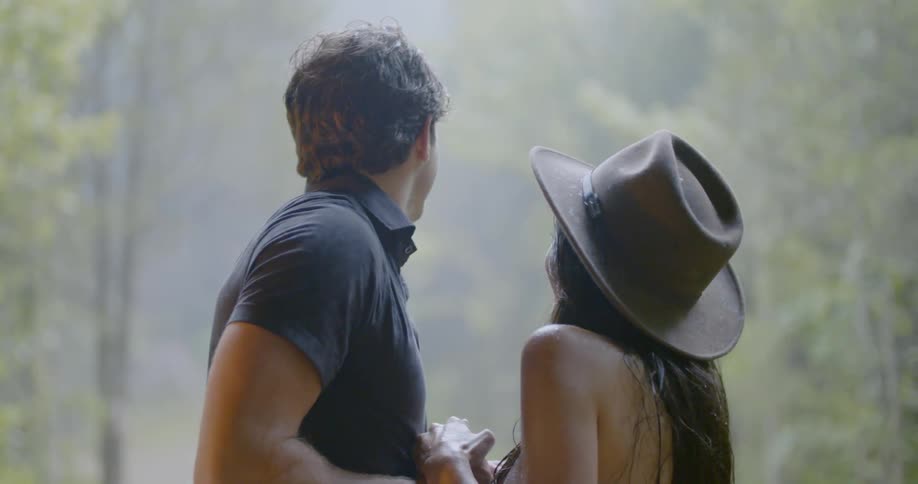 Man and woman hold hands and look out at the rain
