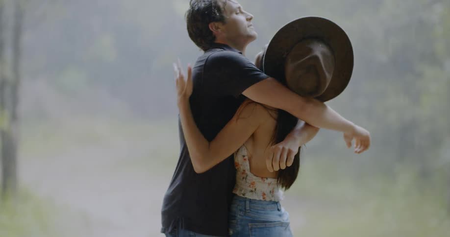 A man and woman are hugging as they stand outside in a rain shower during the day