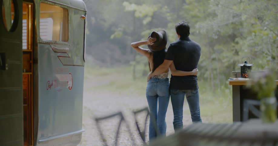 A woman clutches her hat as she stands outside with a man while it rains