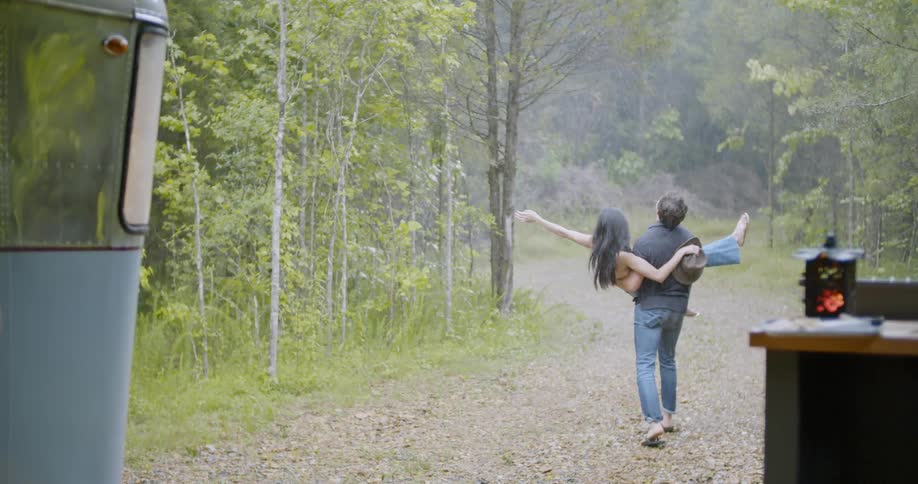 Man carries woman down stony road in the woods while it rains